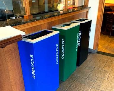 Three bins are shown in an office, one for compost, one for recycling, one for trash.