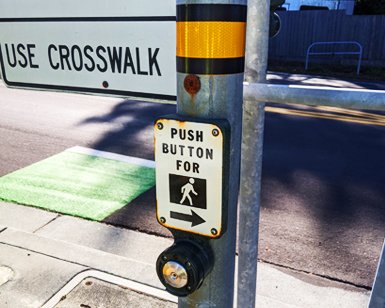 A closeup view of a streetlight pole with a button and sign that says "Press button to cross."