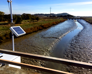 A tide gauge is shown attached to a bridge that spans Novato Creek at Rowland Way.