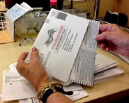 A close-up view of two hands holding a ballot envelope and one of the hands pulling out the ballot.
