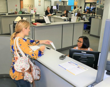 A female clerk (right) at a DMV office assists a female customer (left)