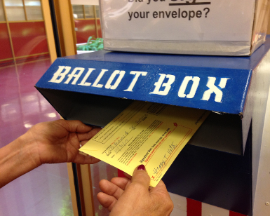 Hands of a voter are shown putting a ballot into a ballot box.