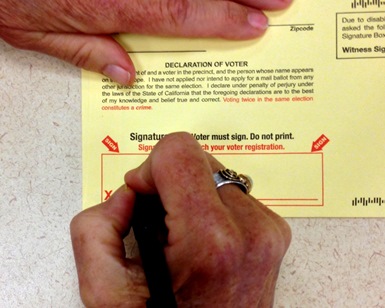 A close-up of a hand with a pen, depicting a person signing a ballot.