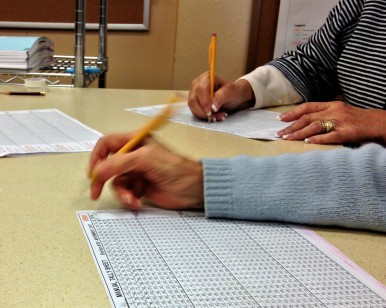 A closeup view of hands with pencils marking down tally numbers on a sheet of paper.