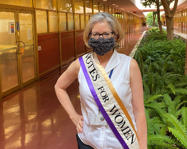 Marin County Registrar of Voters Lynda Roberts stands outside the elections office with a sash across her chest that says Votes For Women.