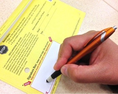 A closeup view of a person's hand signing a ballot envelope.