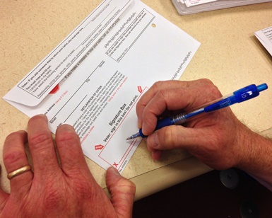A closeup view of a man's hands as he signs a ballot envelope.