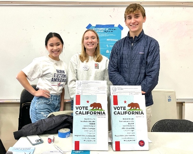 Two young women and one young man pose at a voter registration table