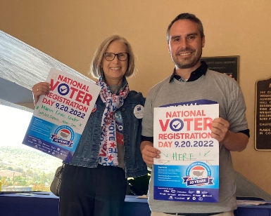 A woman and a man hold up posters outside the Marin County Civic Center to promote Voters' Choice Act Day.