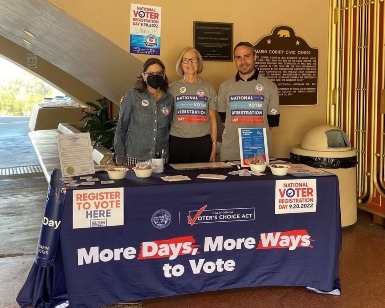 Three elections employees stand behind a table display on National Voter Registration Day