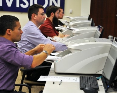 Four men sit behind voting stations and test the equipment.