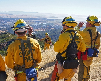 Firefighter trainees get a briefing about a controlled burn by a battalion chief while standing on a ridgetop overlooking a Marin County neighborhood.