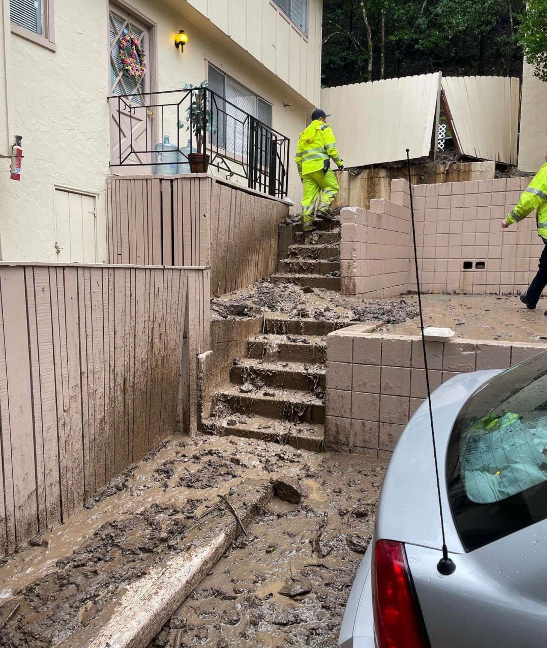 A firefighter walks up the exterior stairs at an apartment complex covered in mud from a storm.