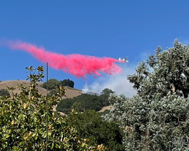 A view from the ground of a firefighting airplane dropping retardant on a wildfire.