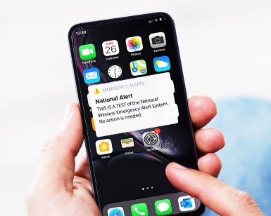 A closeup view of a person's hands holding a cell phone that has an emergency alert notification on the screen