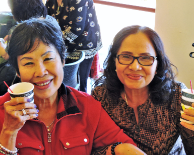 Two smiling senior women hold up their coffee cups.