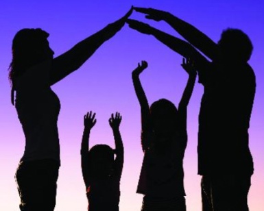 A family is silhouette, with parents forming an arch with their arms and small kids underneath with arms raised high.