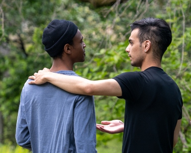 Two young men speak with each other, one holding his hand out asking for understanding or making a point to the other.