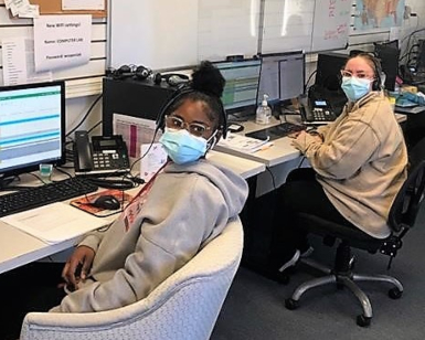 Two female workers sitting at desks and wearing face coverings while working at a COVID-19 call center.