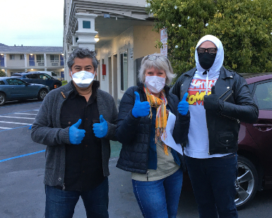 Three people wearing protective masks give thumbs-up signs while working at a motel that has been converted to a homeless shelter.