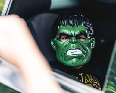 A child wears an Incredible Hulk mask while sitting in a car