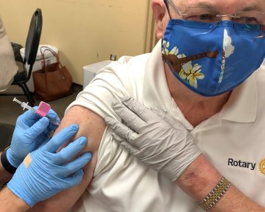 A closeup view of a nurses' hands giving a COVID-19 vaccine to an older man holding up his sleeve.