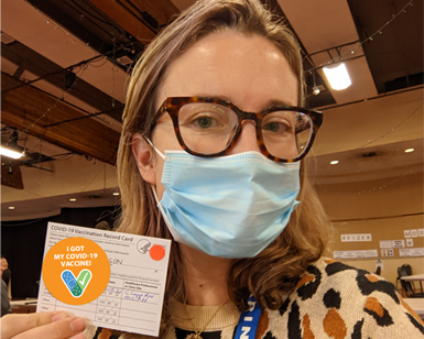Marin County Health and Human Services worker Alison Sexauer holds up her COVID-19 vaccination card while wearing a face covering.
