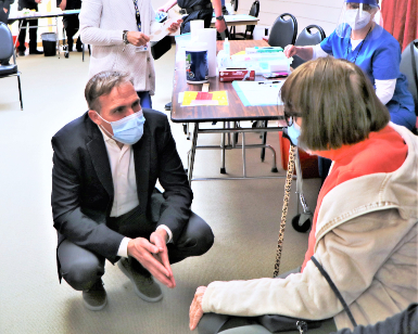 Dr. Matt Willis, Marin County Public Health Officer, kneels down to speak to a seated woman at a COVID-19 vaccination clinic.