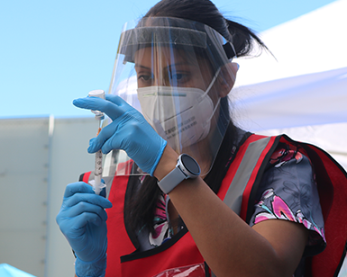 A person wearing protective gear looks at a dose of the COVID-19 vaccine.