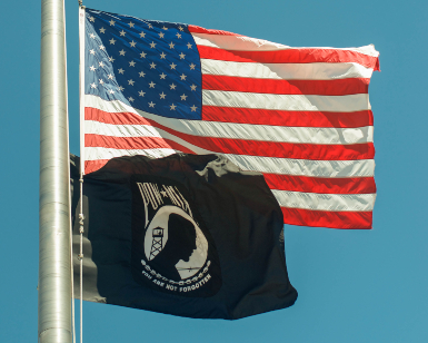 A view of an American flag flying with a Prisoner of War flag