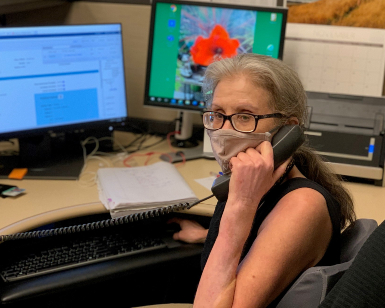 Brijette Overby of the Marin County Veterans Service Office staff answers a phone at her desk while wearing a face covering.