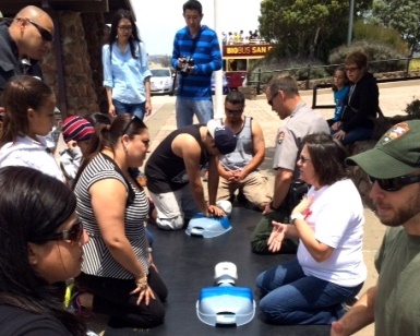 CPR instructors on the left and CPR trainees on the right as one person practices on a human-shaped dummy in the middle.