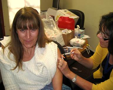 A woman smiles as she receives a flu shot from a nurse.