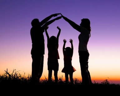 A silhouette of two parents and two children standing in the grass at dusk.
