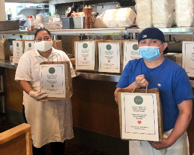 Two cooks at Iron Springs Pub & Brewery show bags of packaged food that will be delivered to Great Plates Program recipients.