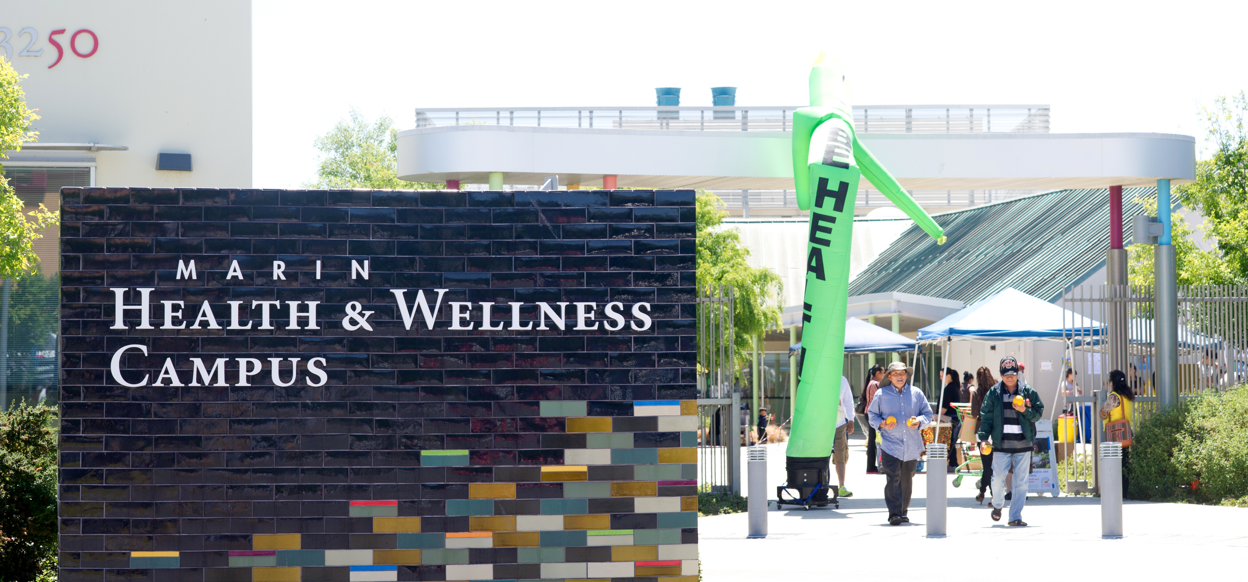 People walk past the large sign saying Marin County Health and Wellness Campus during the Fruit and Veggie Festival.
