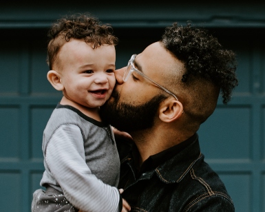 A man kisses his son of about 1 year old while holding him.