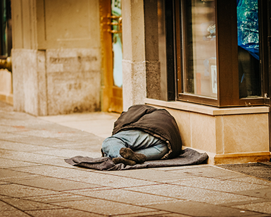 A individual who is homeless sleeps on a sidewalk