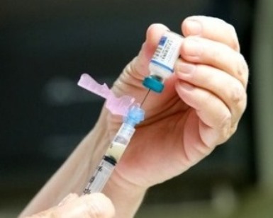 A close-up of a nurse's hands preparing a needle for an immunization shot.
