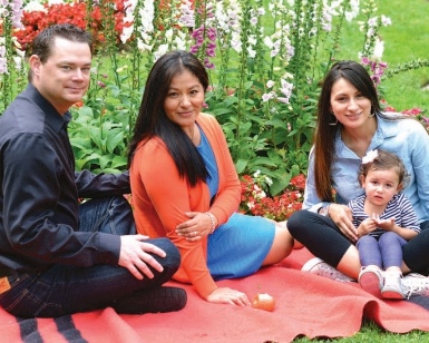 A Latino family of five sits on a blanket in a garden