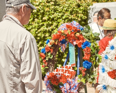 A man with his back turned to the camera looks at a flower arrangement in front of a military monument.