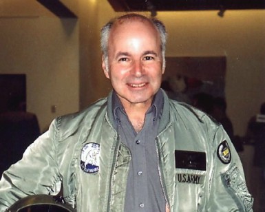 Tony Lazzarini, wearing a flight jacket and holding a helicopter crew helmet