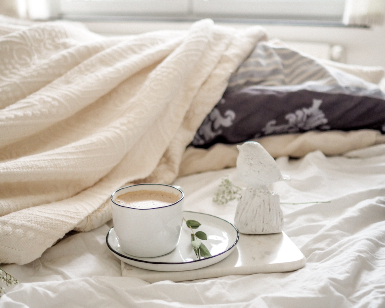 A photo of a cup of coffee sitting on a tray on a bed.