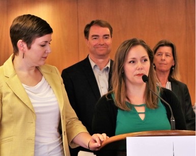 Ashley Hart McIntyre speaks at a news conference about homelessness with other people in the background. 