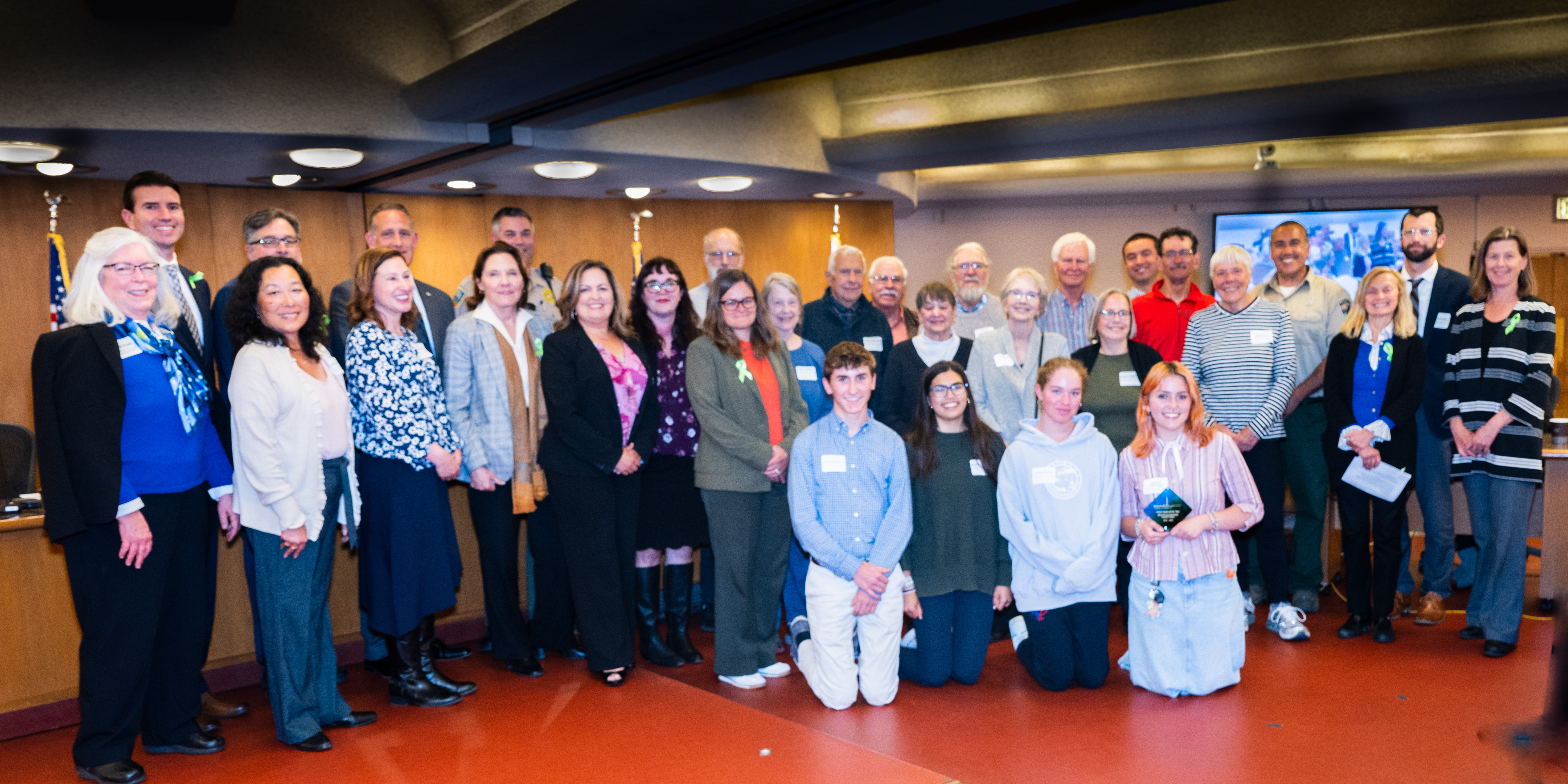 Group photo of about 25 people posing at a Board of Supervisors meeting