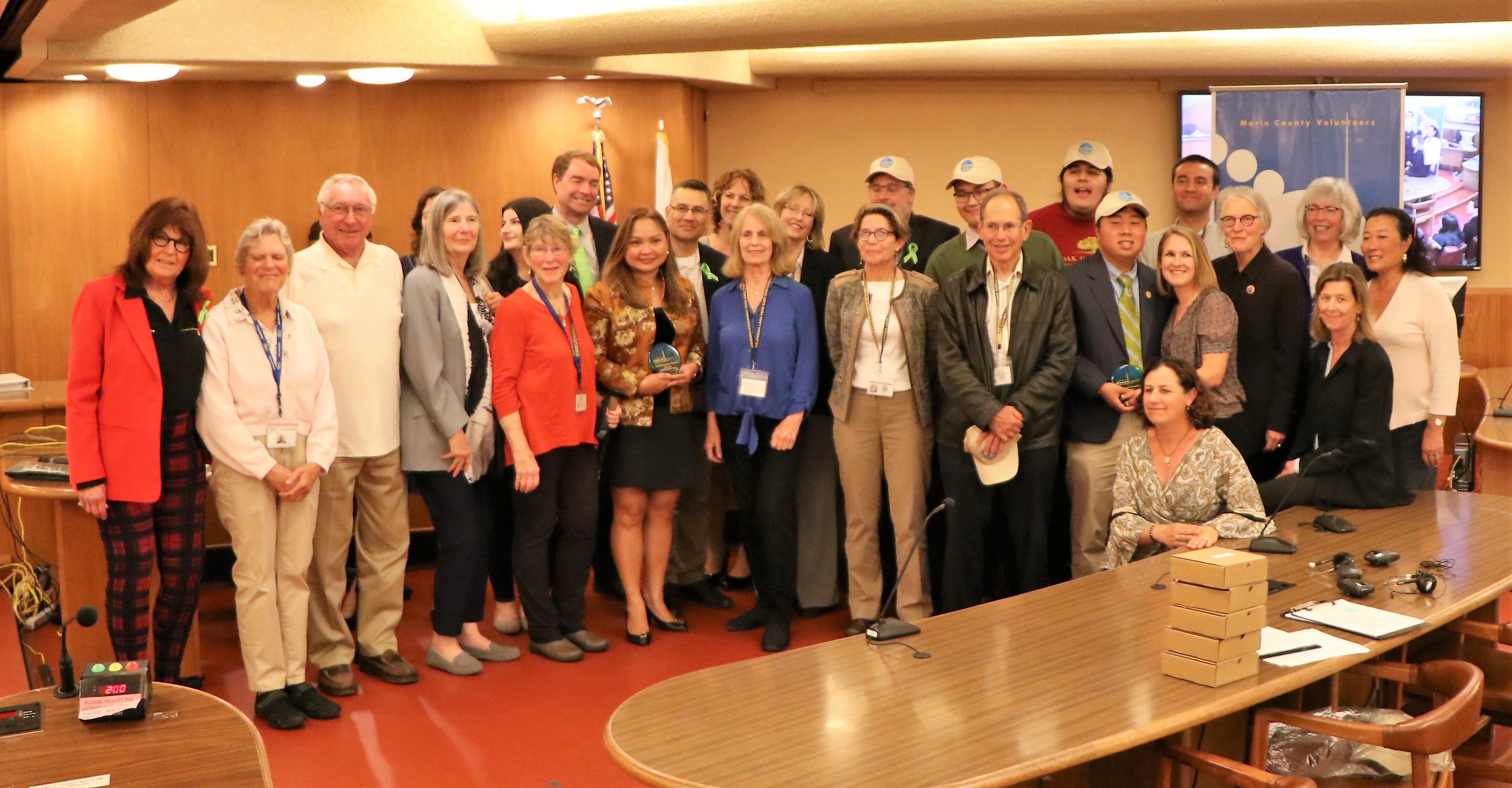 A group of about 25 volunteers and interns gather for a photo during the Board of Supervisors meeting.