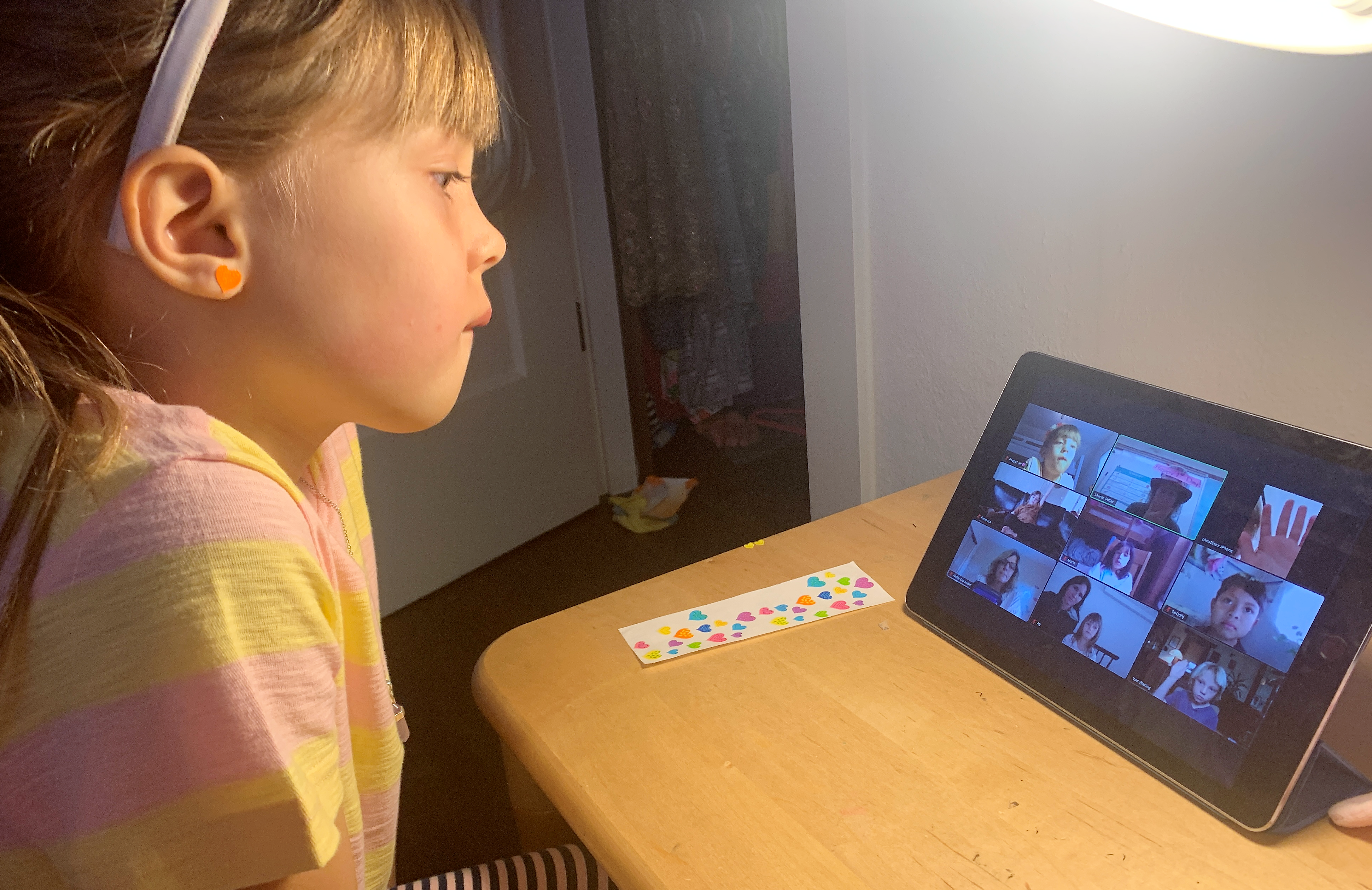 A girl of about 6 years old looks at an iPad as she participates in an online learning session.