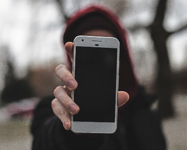 A young woman, obscured, holds up a smartphone toward the camera.