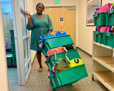 Ramona Little Taylor of Marin County Free Library poses with several boxes full of stuffed backpacks that will be given away to kids.