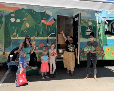 Young kids stand with adults and library workers outside the Bookmobile.